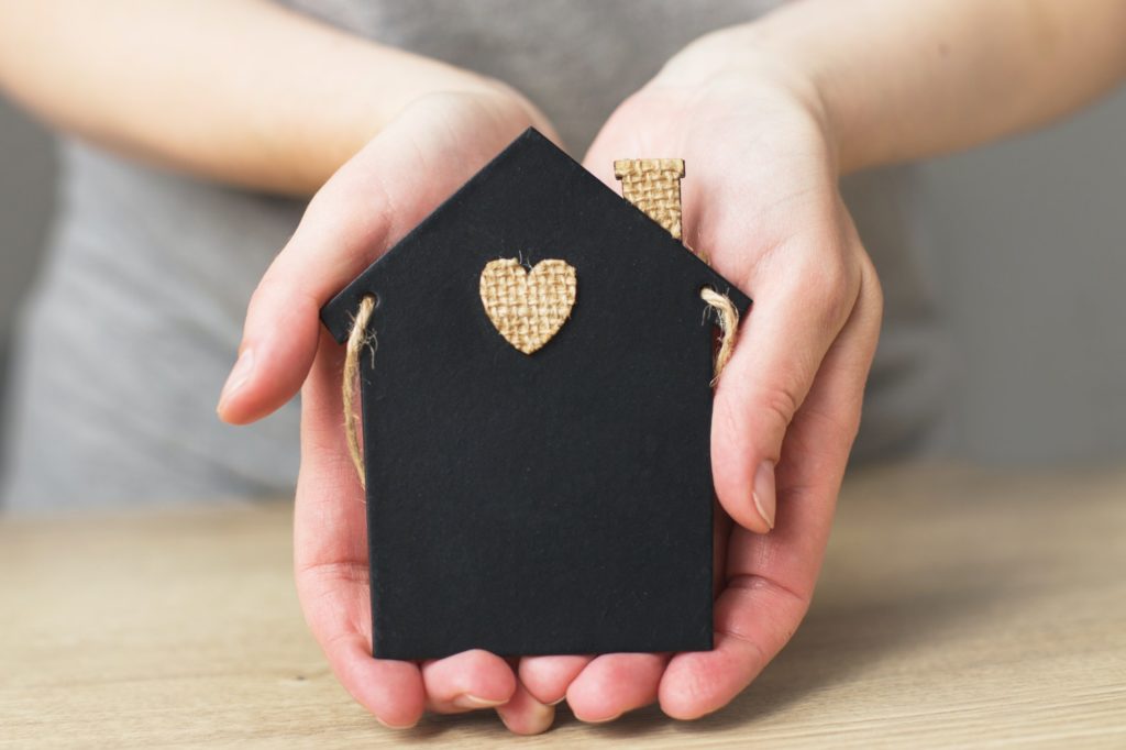 womans hand holding little toy house. Home insurance concept.
